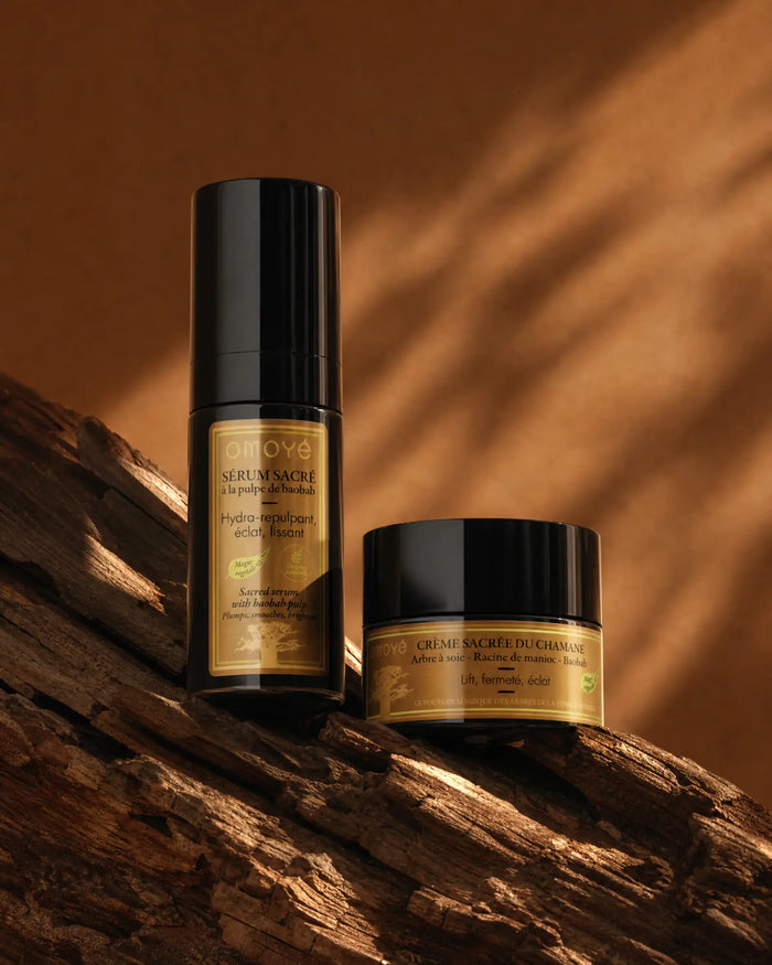 Sérum Sacré à la pulpe de Baobab et Crème Sacrée du chamane dressés sur un bois flotté, ombres de feuillage, fond terracotta