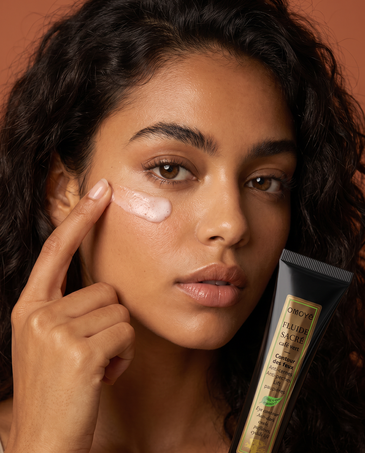 Femme appliquant le Fluide Sacré au Café Vert Omoyé sous l'œil, soin contour des yeux anti-cernes et anti-poches
