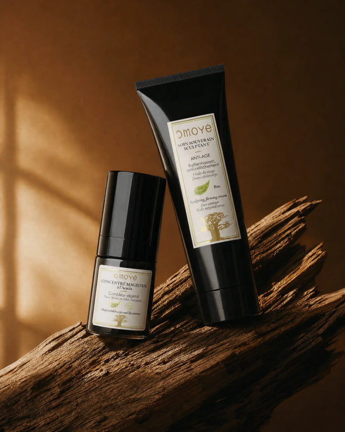 Rituel Magistral Ciblé Omoyé : le Concentré Magistral à l'Acacia et le Soin Souverain Sculptant au Moringa posés sur bois, fond terracotta