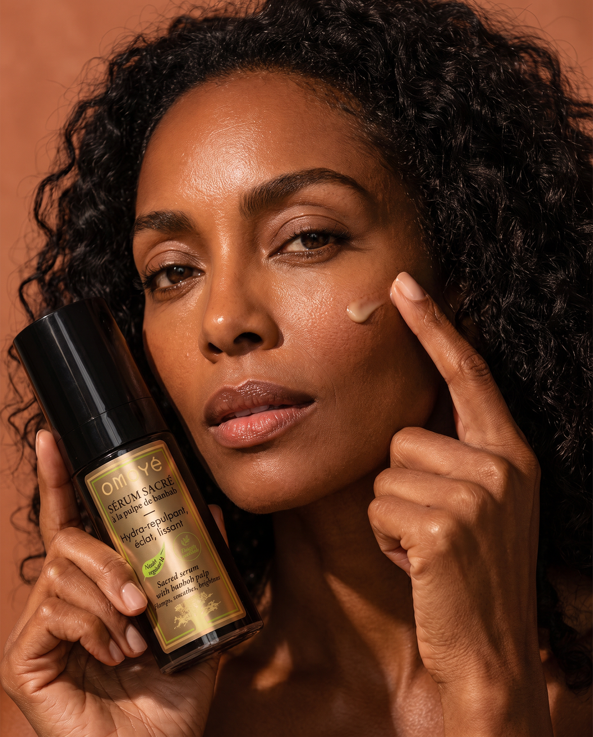 Femme appliquant une goutte du Sérum Sacré à la pulpe de baobab Omoyé sur sa joue, sérum visage hydra-repulpant