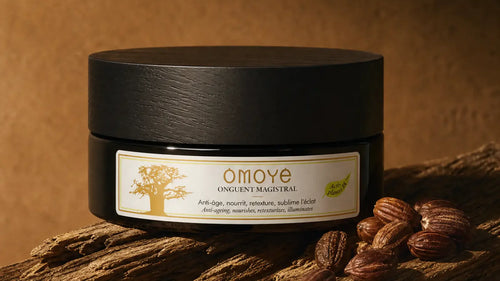 Pot de l'Onguent Magistral Omoyé posé sur un bois flotté à côté de graines de jojoba, fond terracotta