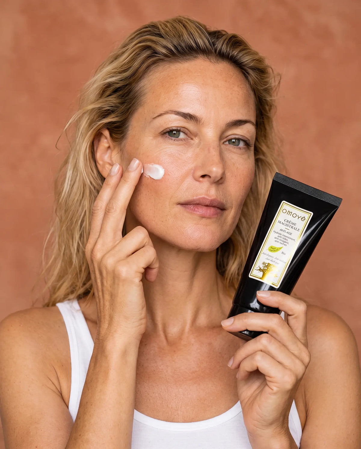 Femme à la peau mature appliquant la Crème Magistrale Omoyé sur sa joue, soin visage anti-âge bio