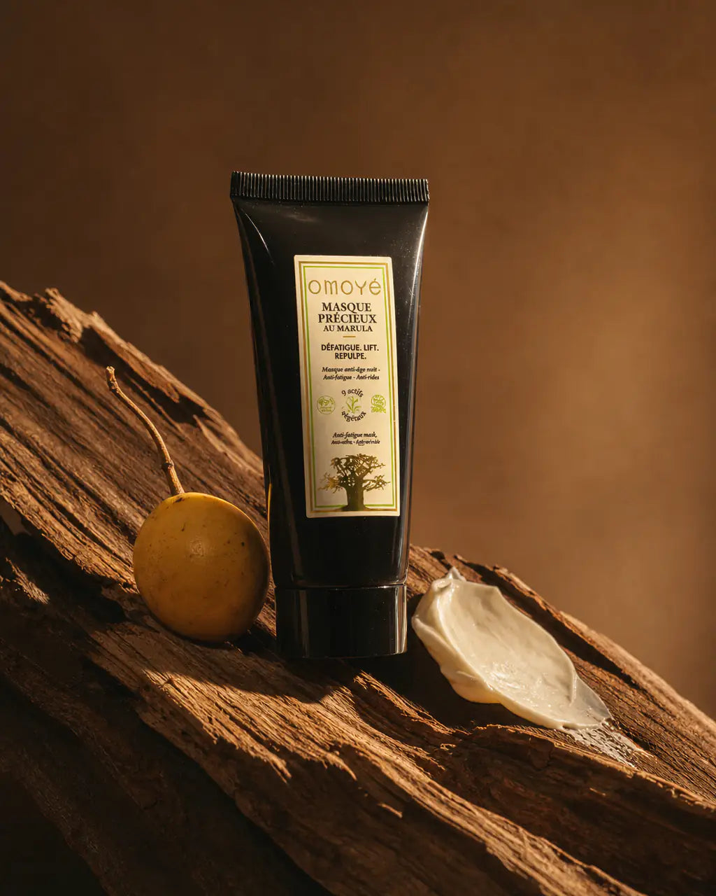 Le Masque Précieux au Marula Omoyé et son arbre totem, fruit de marula et touche de texture posés sur bois, fond terracotta