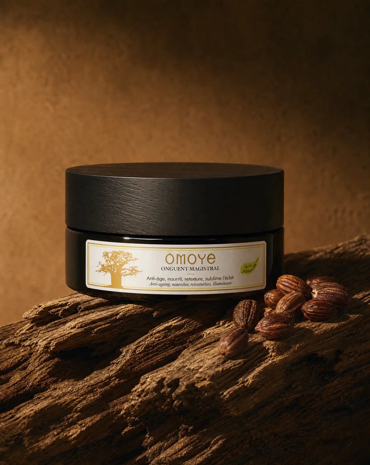 Onguent Magistral posé sur un bois flotté à côté de graines de jojoba, fond terracotta